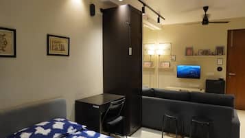 Un espacio habitable pequeño con cama, escritorio, sofá, televisor y un taburete.