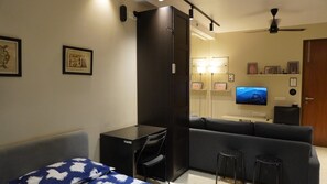A compact living space with a bed, a desk, a sofa, a TV, and a small stool. - Egyptian Studio_Hiranandani Estate_Balcony (Thane)