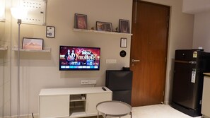 A compact living space with a television mounted on the wall, a small table, a refrigerator, and a door. - Egyptian Studio_Hiranandani Estate_Balcony (Thane)