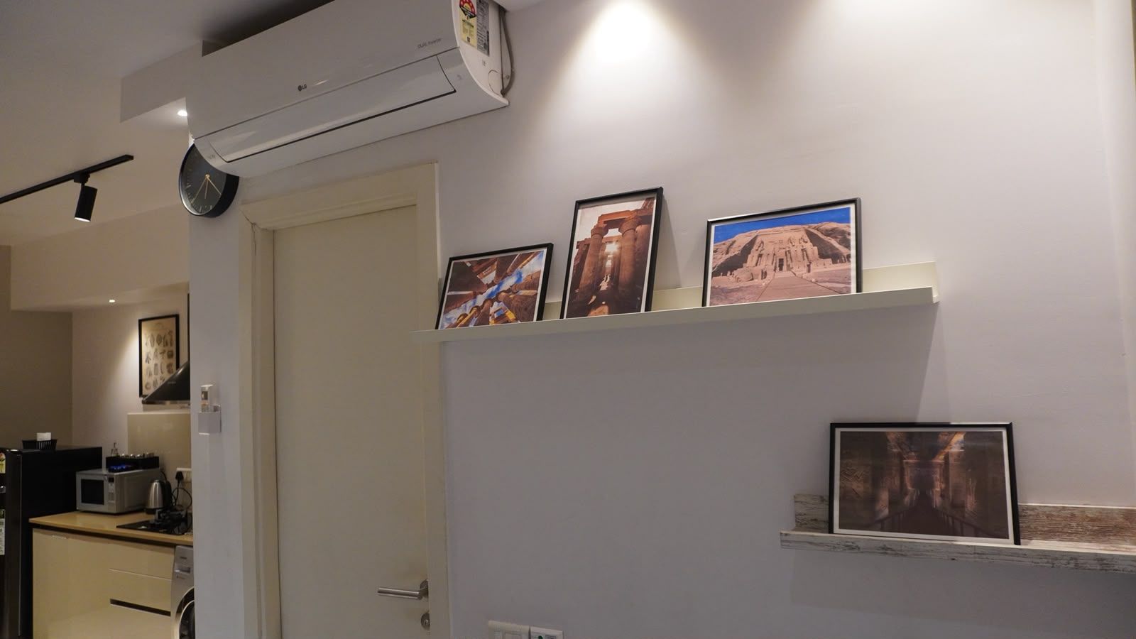 A hallway with a door, a wall-mounted air conditioner, and a shelf with framed pictures.