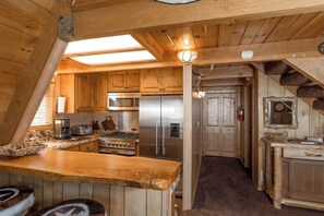 Un intérieur en bois avec une cuisine équipée d’appareils électroménagers en acier inoxydable, un plan de travail en bois et un plafond en pente agrémenté de lucarnes.