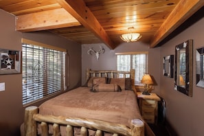 Ein Schlafzimmer mit einem Bettgestell aus Holz, einem Hirschschädel als Kopfteil und einem Fenster mit Jalousien.