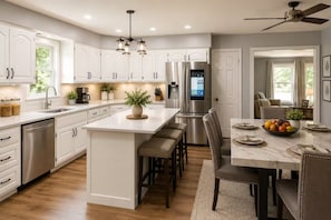 Una cocina moderna con armarios blancos, una isla central, electrodomésticos de acero inoxidable y un comedor con mesa de mármol.