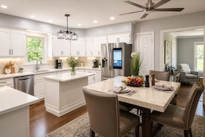 Una cocina moderna con armarios blancos, una isla central y un comedor con una mesa preparada para dos.