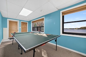 Ein Zimmer mit einem Tischtennis-Tisch, zwei Türen und einem Fenster mit Blick auf ein Gew ässer.