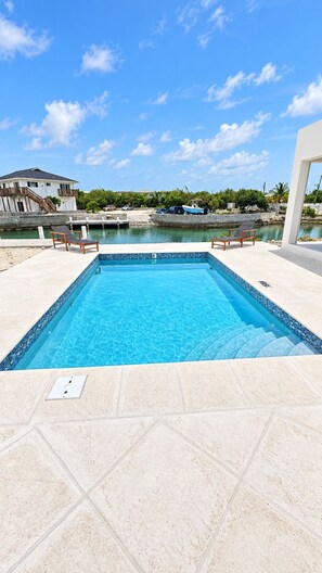 A swimming pool with clear blue water, surrounded by a tiled deck. - Newly Listed -Canal front 2-bedroom Villa (Providenciales)