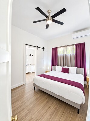 A hotel room with a bed, a ceiling fan, a bathroom visible through an open door, and a window with curtains. - Newly Listed -Canal front 2-bedroom Villa (Providenciales)