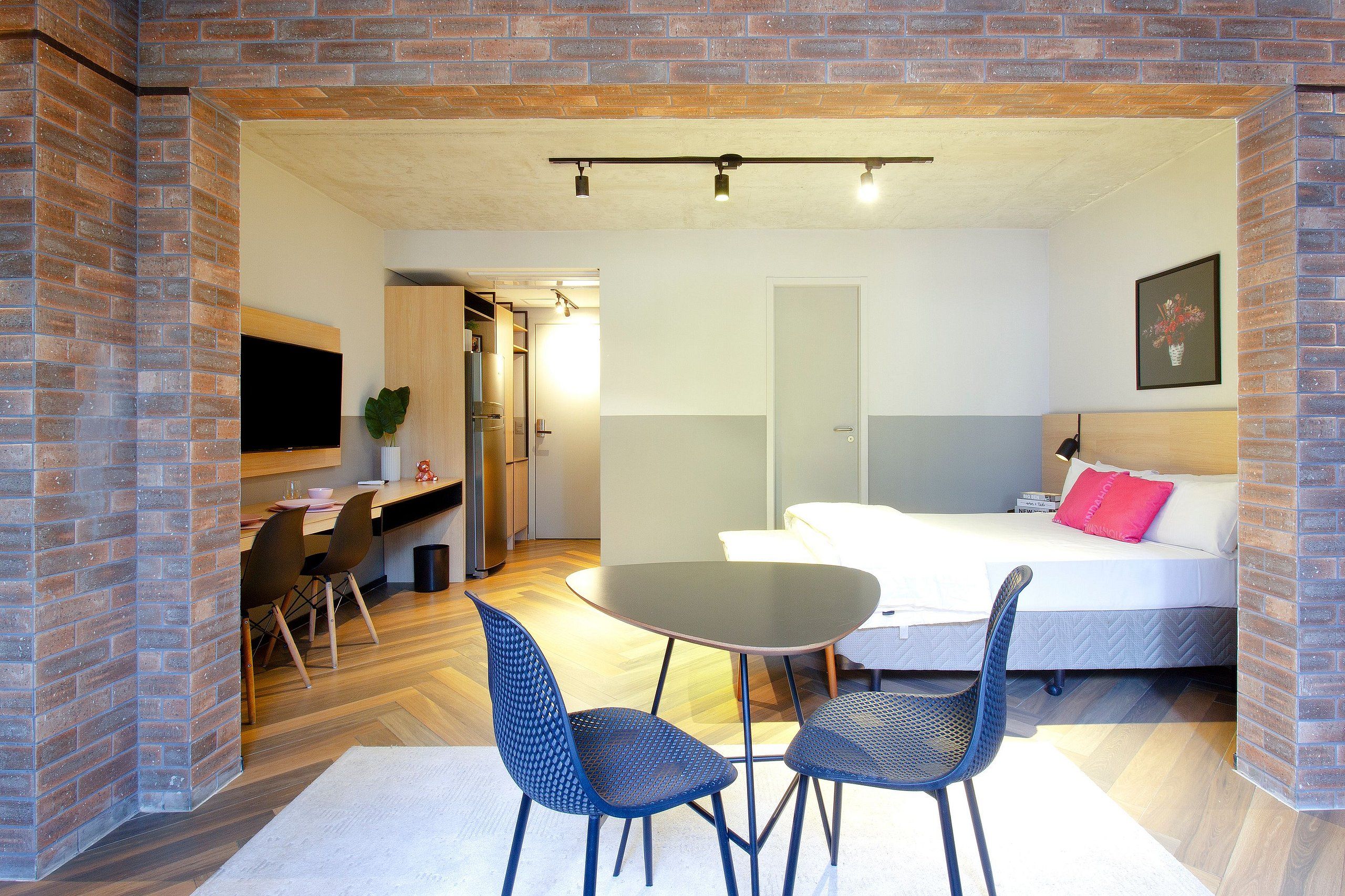 Habitación de hotel con cama, escritorio, dos sillas, televisor y puerta que da a otra habitación.