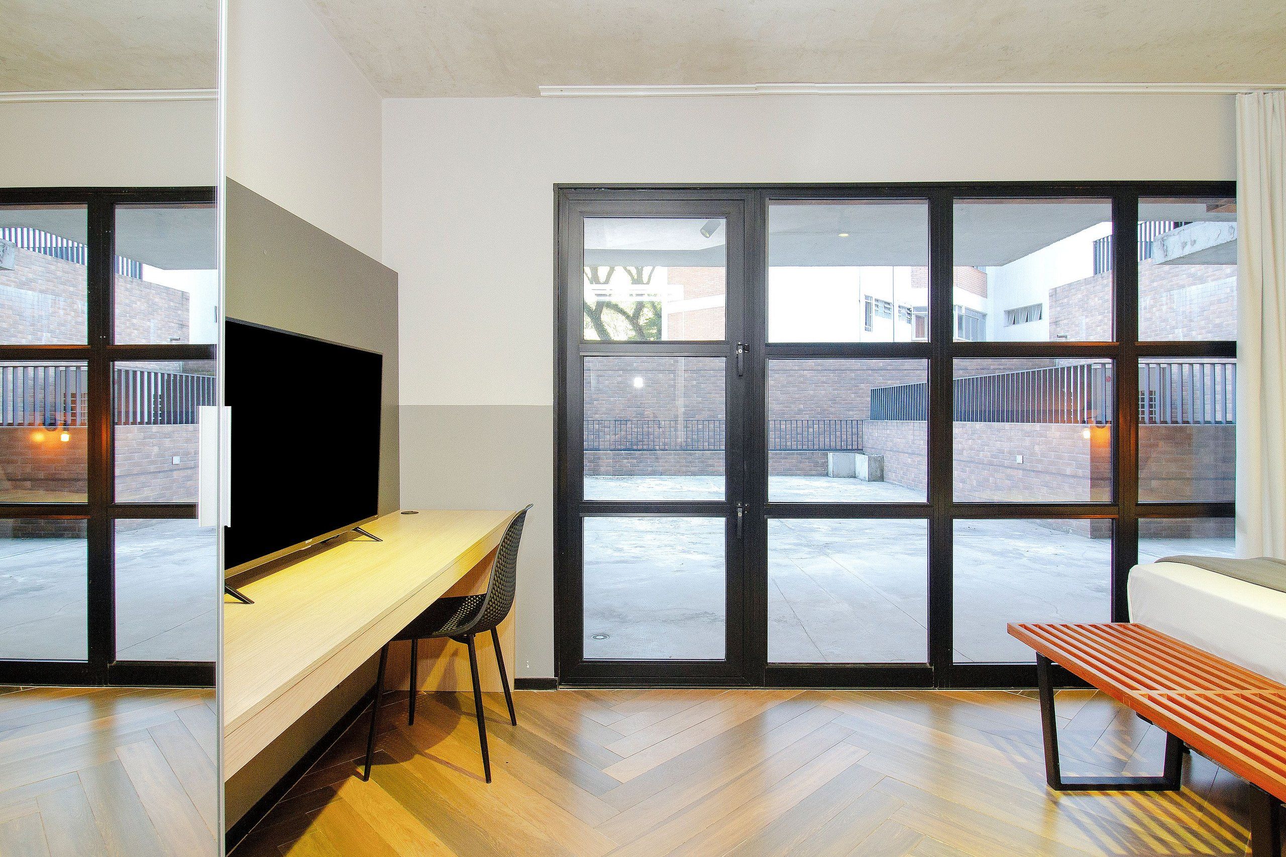 Ein modernes Zimmer mit einer großen Schiebeglaswand, einem Flachbildfernseher, einem Holztisch, einem Stuhl und einer Bank.