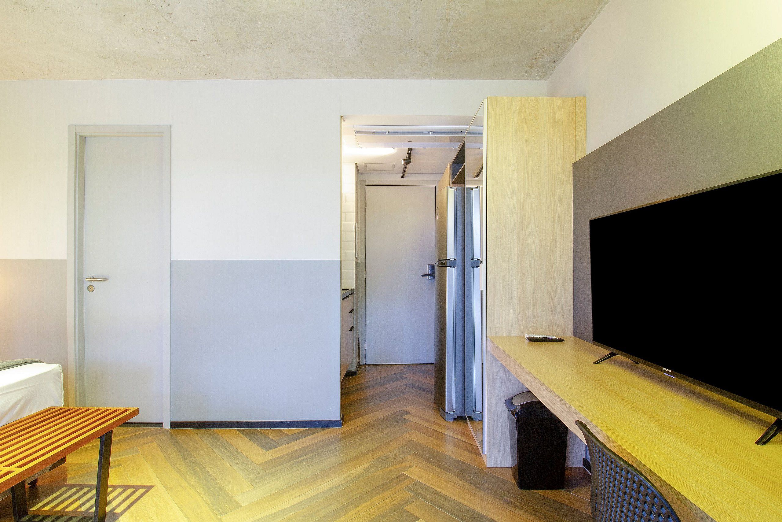 A hotel room with a wooden floor, a TV on a wooden stand, a bed, and a door.