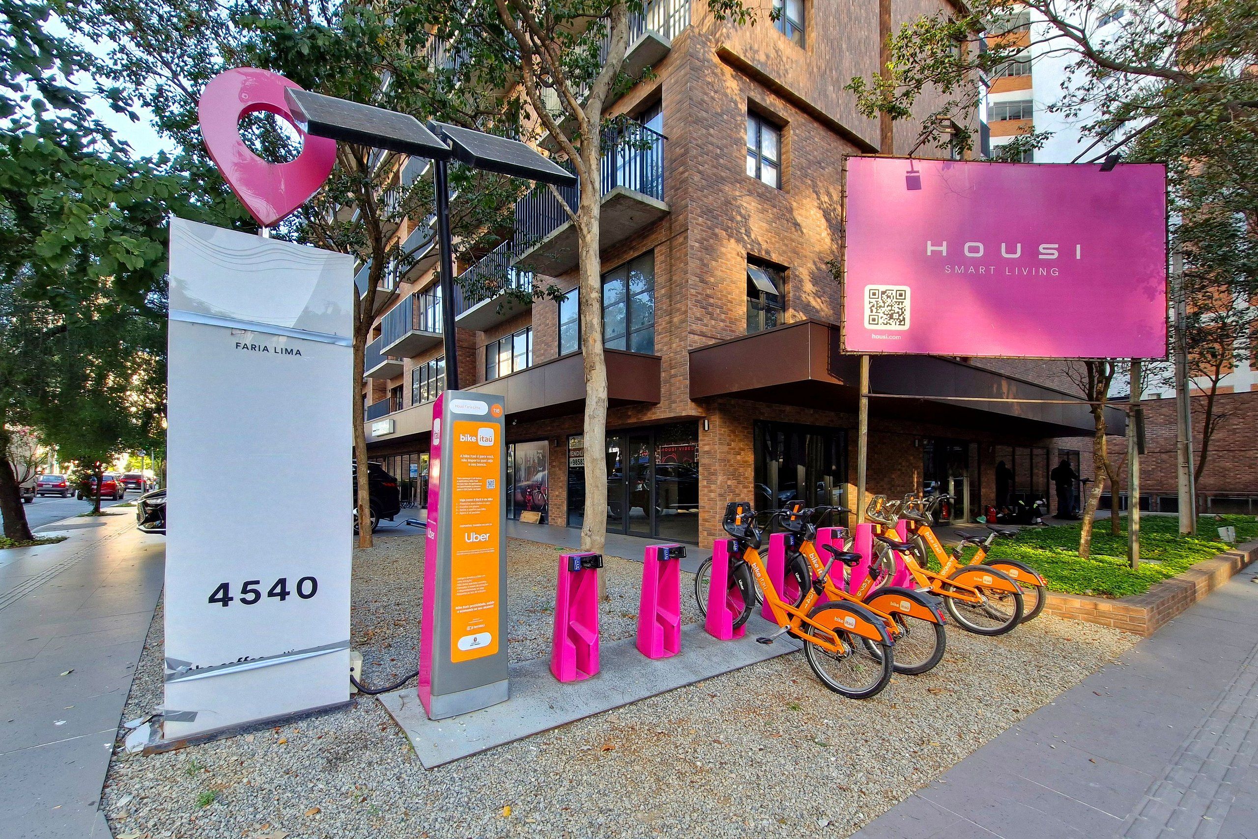 Un bâtiment moderne avec une grande enseigne rose bien visible, qui fait de la publicité pour « HOUZI SMART LIVING ».