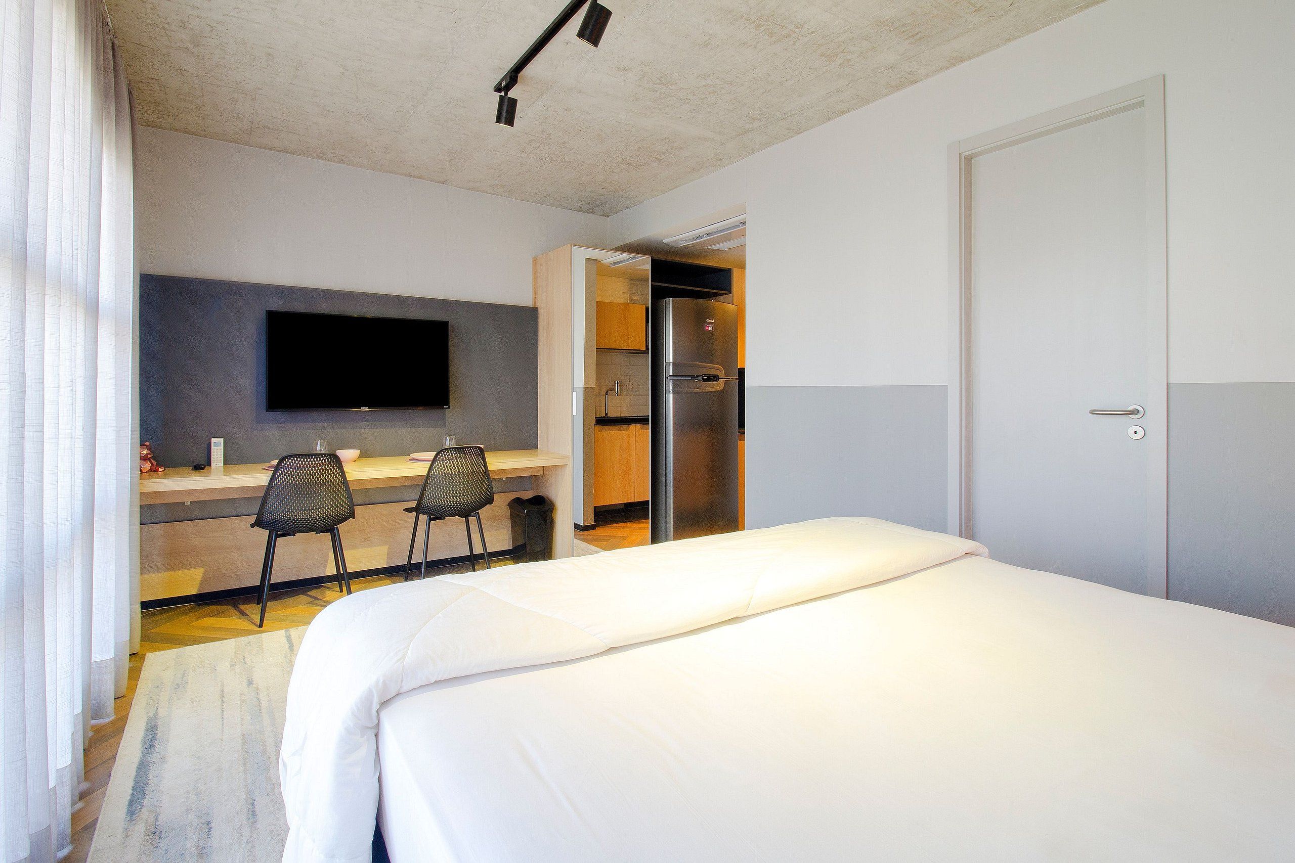 Habitación de hotel con cama, escritorio con sillas, televisor y armario.