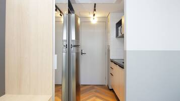 Un pasillo estrecho con una puerta de vidrio que da a una habitación, una puerta blanca al final y una zona de cocina con mostrador y armarios.