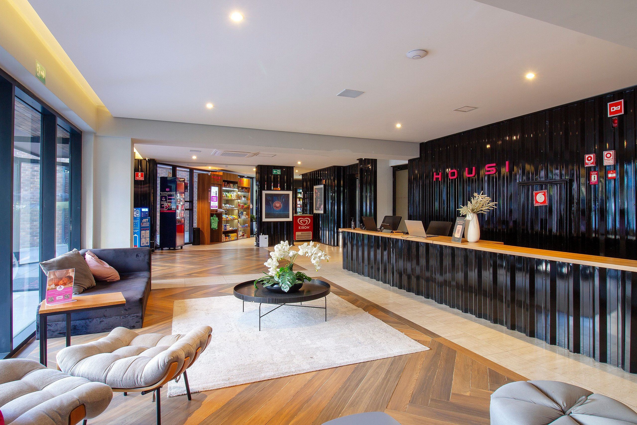 Un área de recepción de hotel con diseño moderno, que incluye un mostrador de recepción, una zona de estar y un amplio ventanal con vistas al exterior.