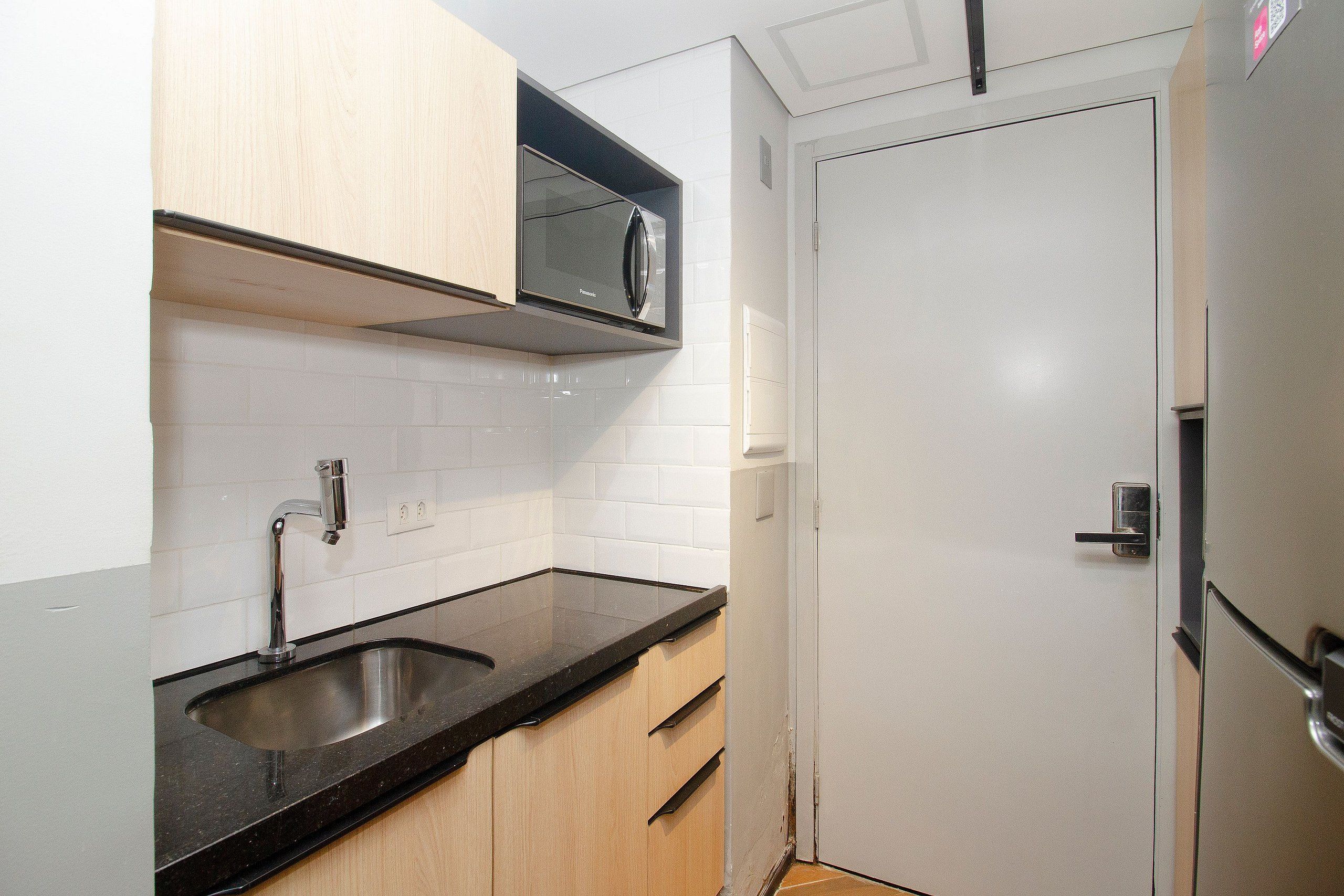 A compact kitchen with a sink, cabinets, and a microwave.