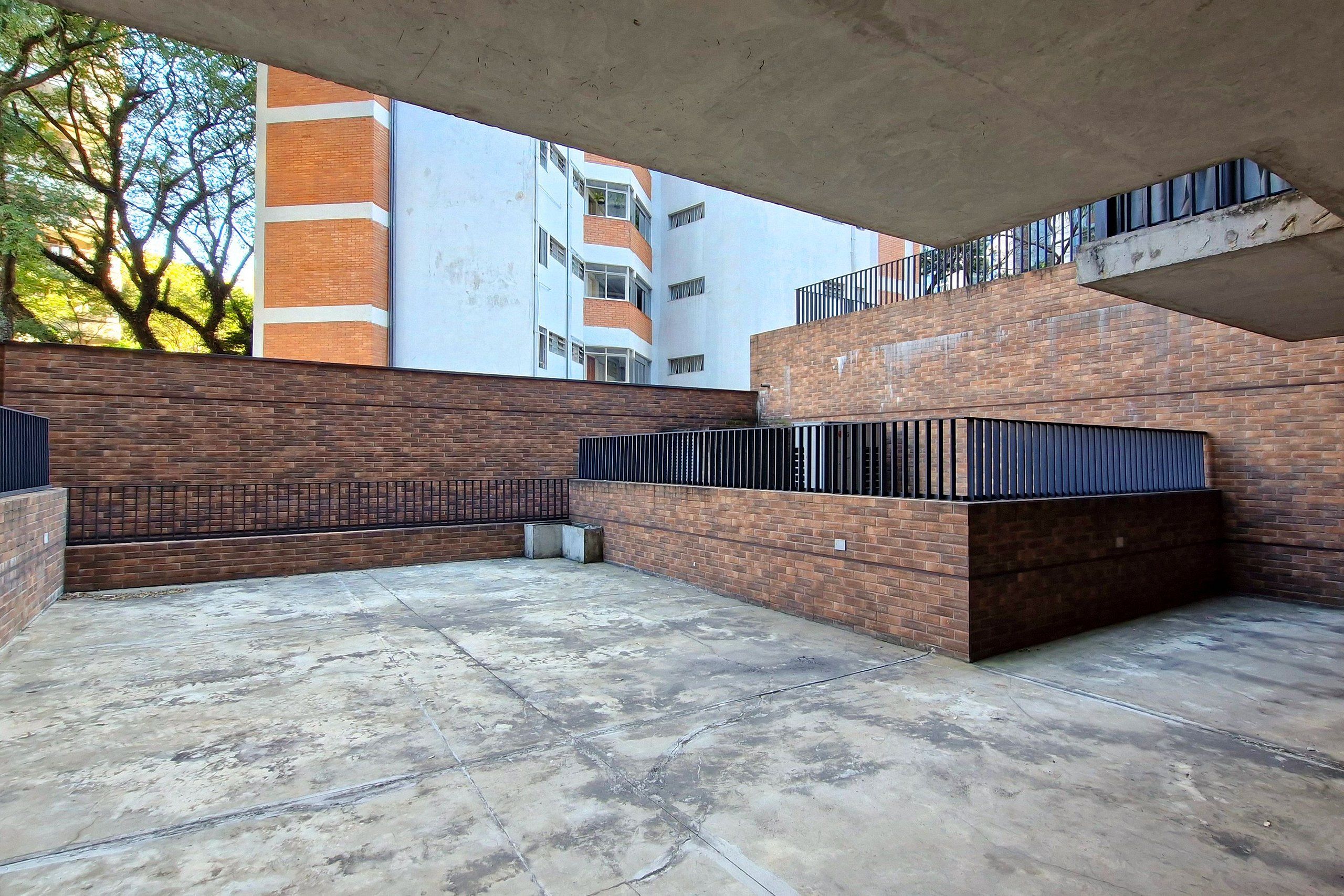 An outdoor patio area with a brick wall, a concrete floor, and a metal railing.