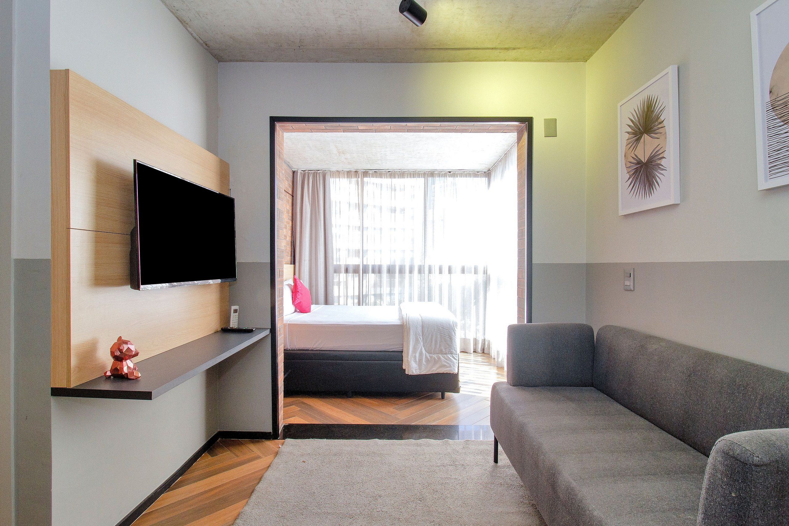 Un salon moderne avec un téléviseur à écran plat fixé au mur, un canapé gris et une étagère en bois.