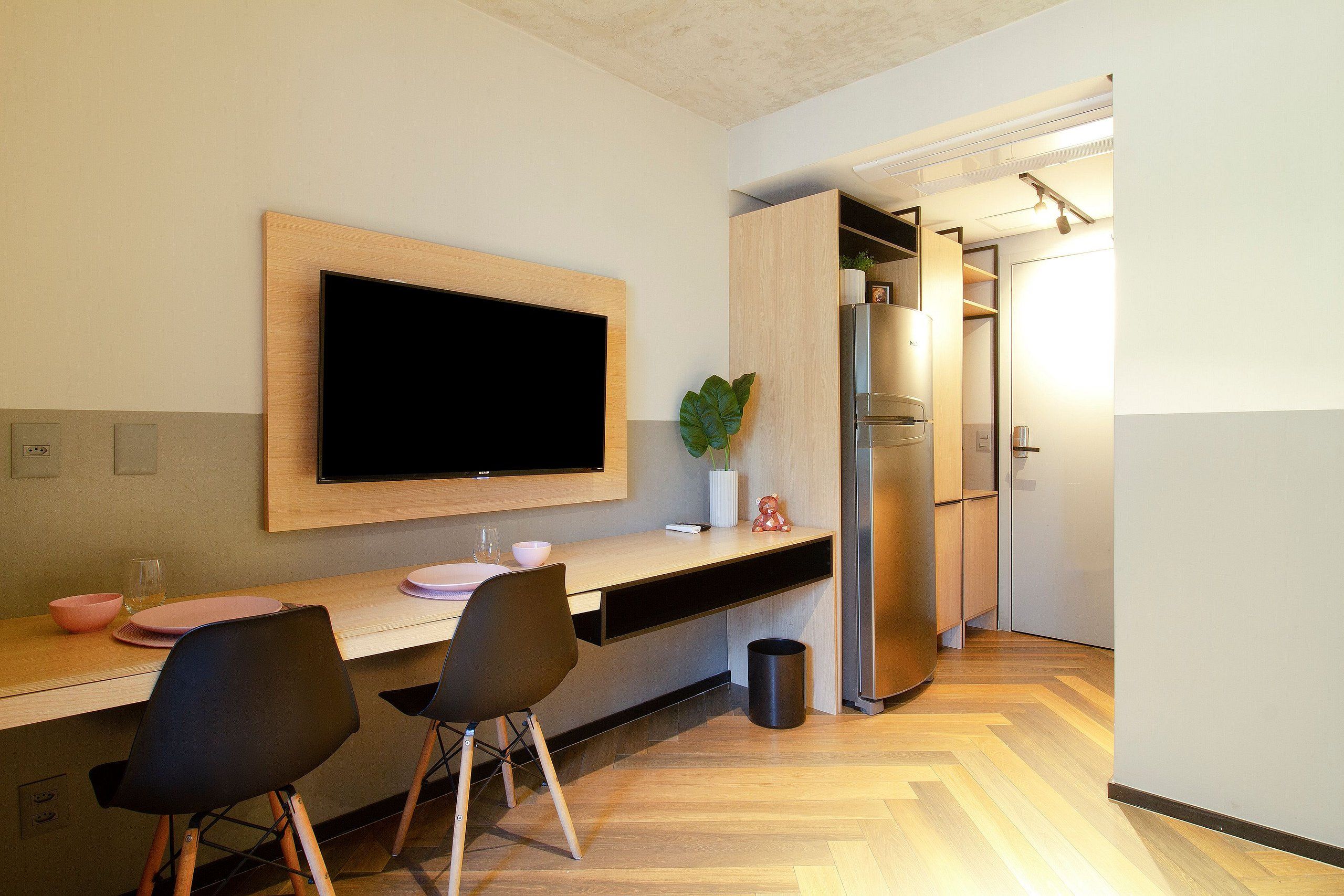 Eine moderne Küche mit Flachbildfernseher, Holztresen, zwei Stühlen, einem Blumentopf und einem Kühlschrank.