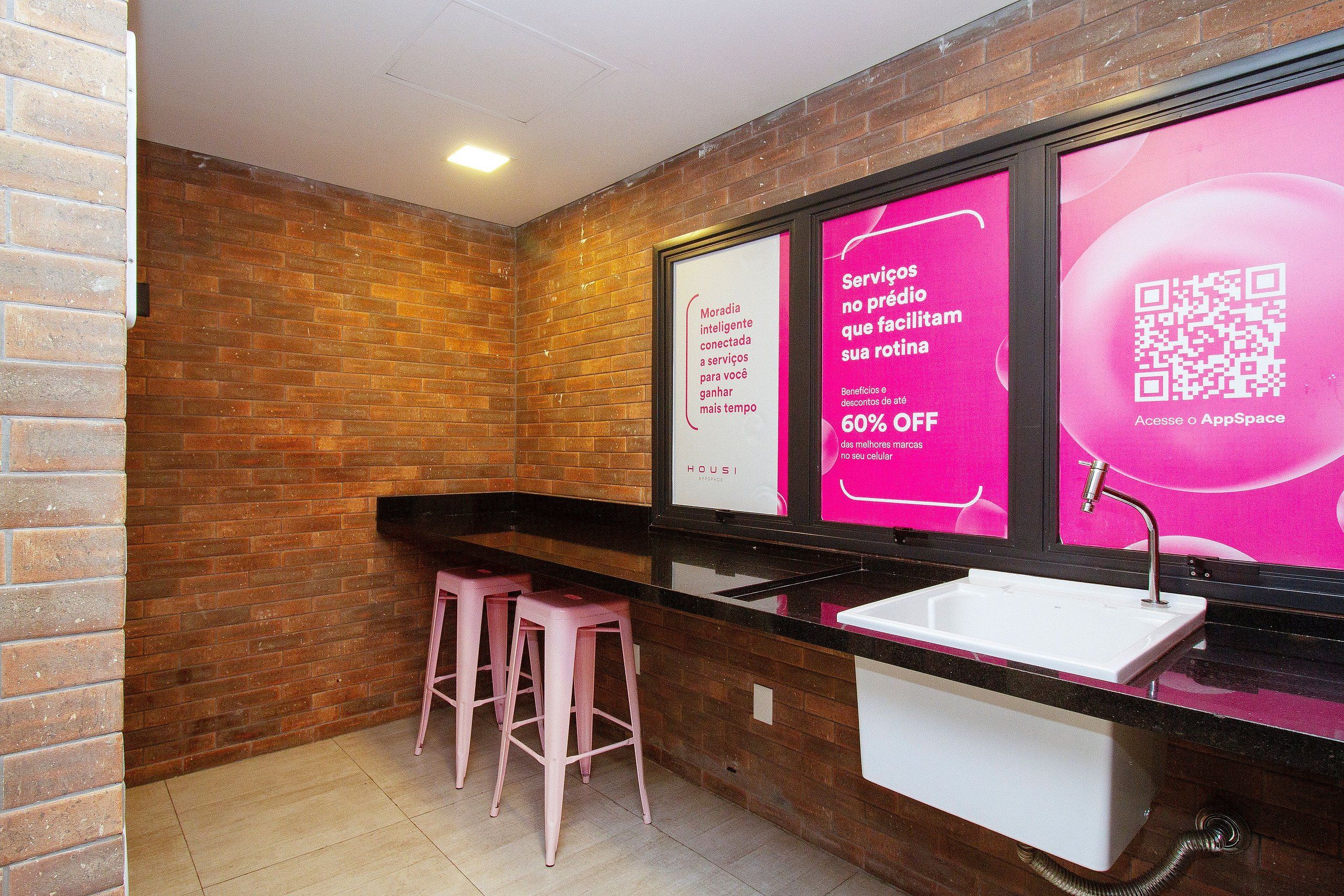 Un baño con pared de ladrillo, un lavamanos y dos taburetes rosados.