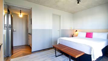 A hotel room with a bed, bedside table, bench, and a small bedside plant.