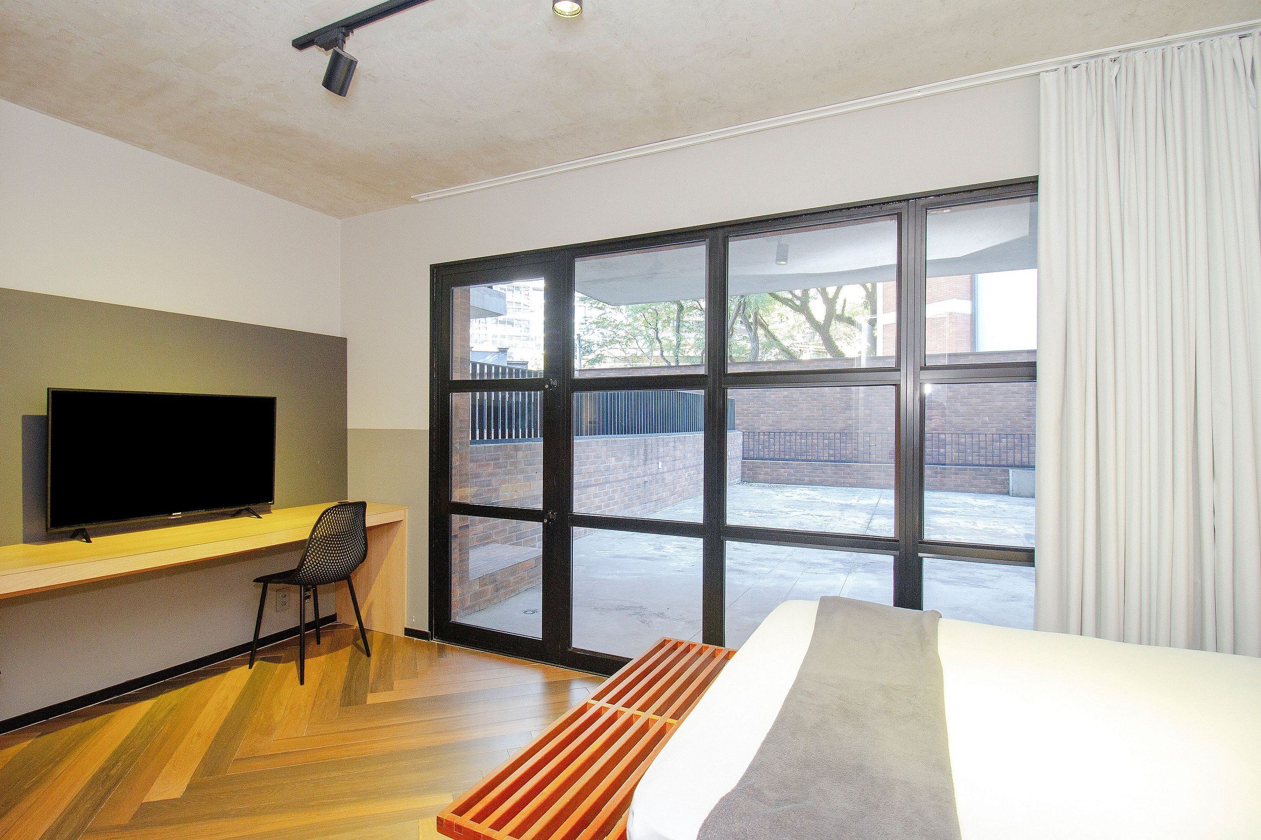 Ein modernes Hotelzimmer mit großem Fenster, Flachbildfernseher, Schreibtisch und Bett.