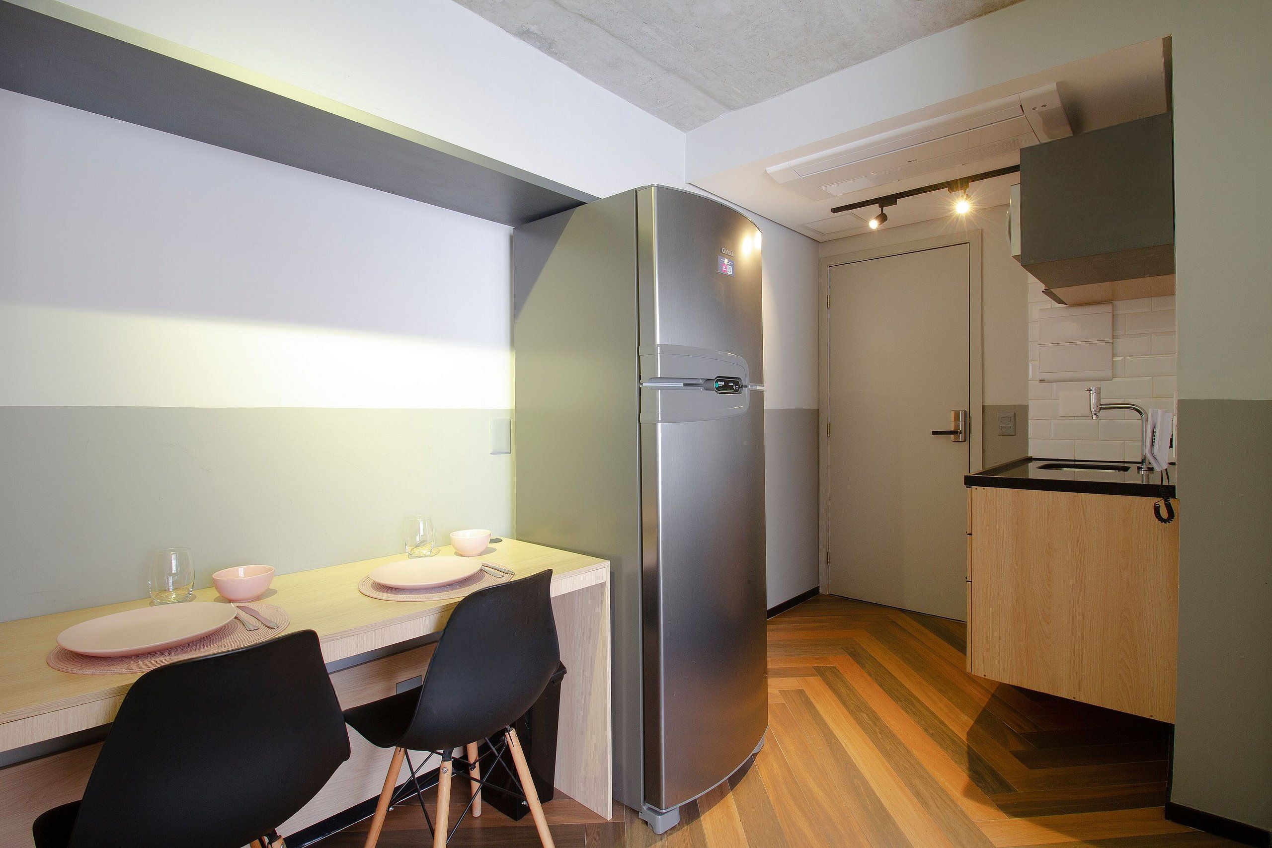 Una cocina compacta con refrigerador incorporado, un comedor con mesa y sillas, y una pequeña encimera con lavamanos.