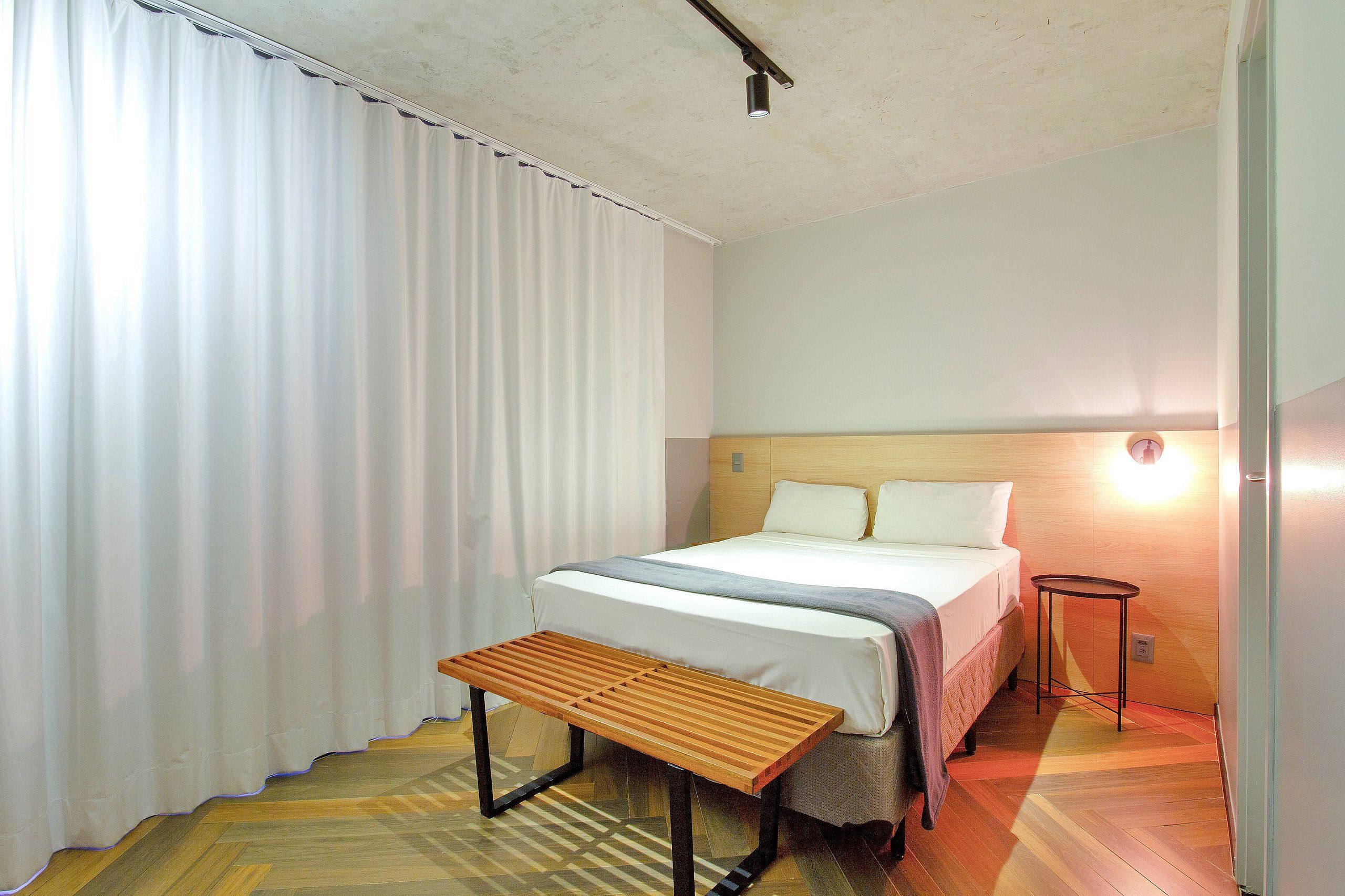 A hotel room with a bed, a bedside table, a lamp, and a window with curtains.