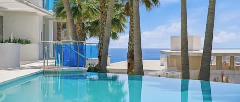 A swimming pool with clear blue water, surrounded by palm trees and a view of the sea.