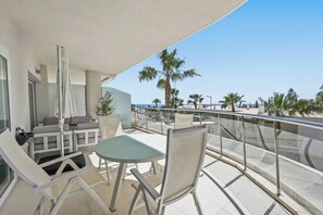 A balcony with outdoor seating, a table, and a view of palm trees and the sea. - Panoramic View by IIM (Benalmádena)