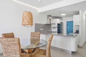 A modern kitchen with a central island, white cabinetry, and a glass-top dining table with wicker chairs. - Panoramic View by IIM (Benalmádena)