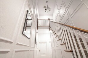 Un pasillo interior blanco con una escalera de madera, un candelabro y una puerta con el número 2.