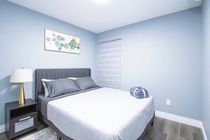 Une chambre à coucher comprenant un lit, une table de chevet, une lampe et une œuvre d’art accrochée au mur.
