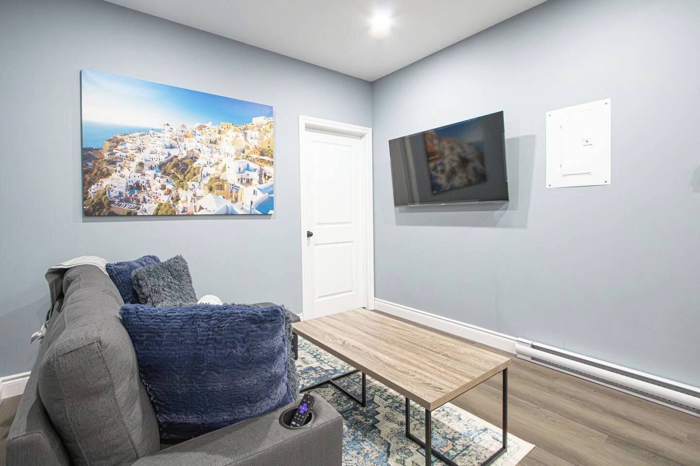A living room with a grey sofa, a wooden coffee table, and a large painting of a coastal town.