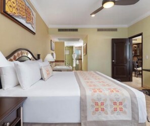 Une chambre d’hôtel comprenant un lit, une table de chevet, un bureau, une chaise, un ventilateur de plafond et une porte donnant sur une autre pièce.