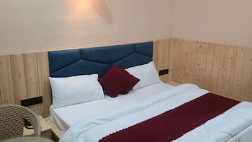 Un letto rifatto con lenzuola bianche e bordeaux, una testiera imbottita blu e un punto luce fissato al muro.
