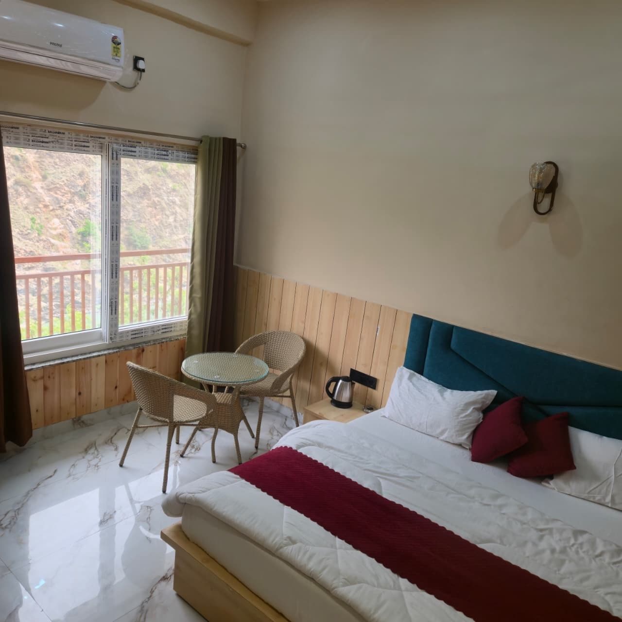 Ein Hotelzimmer mit Bett, kleinem Tisch mit Stühlen, Fenster mit Aussicht und Klimaanlage.
