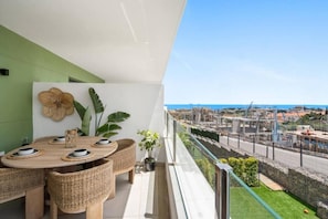 A balcony with a dining set, a potted plant, and a view of a coastal area with construction. - Golden View by IIM (AN)