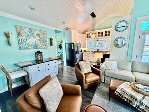 A spacious living room with a sofa, armchairs, and a coffee table. A kitchen with a refrigerator and cabinets is visible in the background. - Cozy Teal site N111 Ocean Lakes home close to everything Ocean Lakes! (Myrtle Beach)