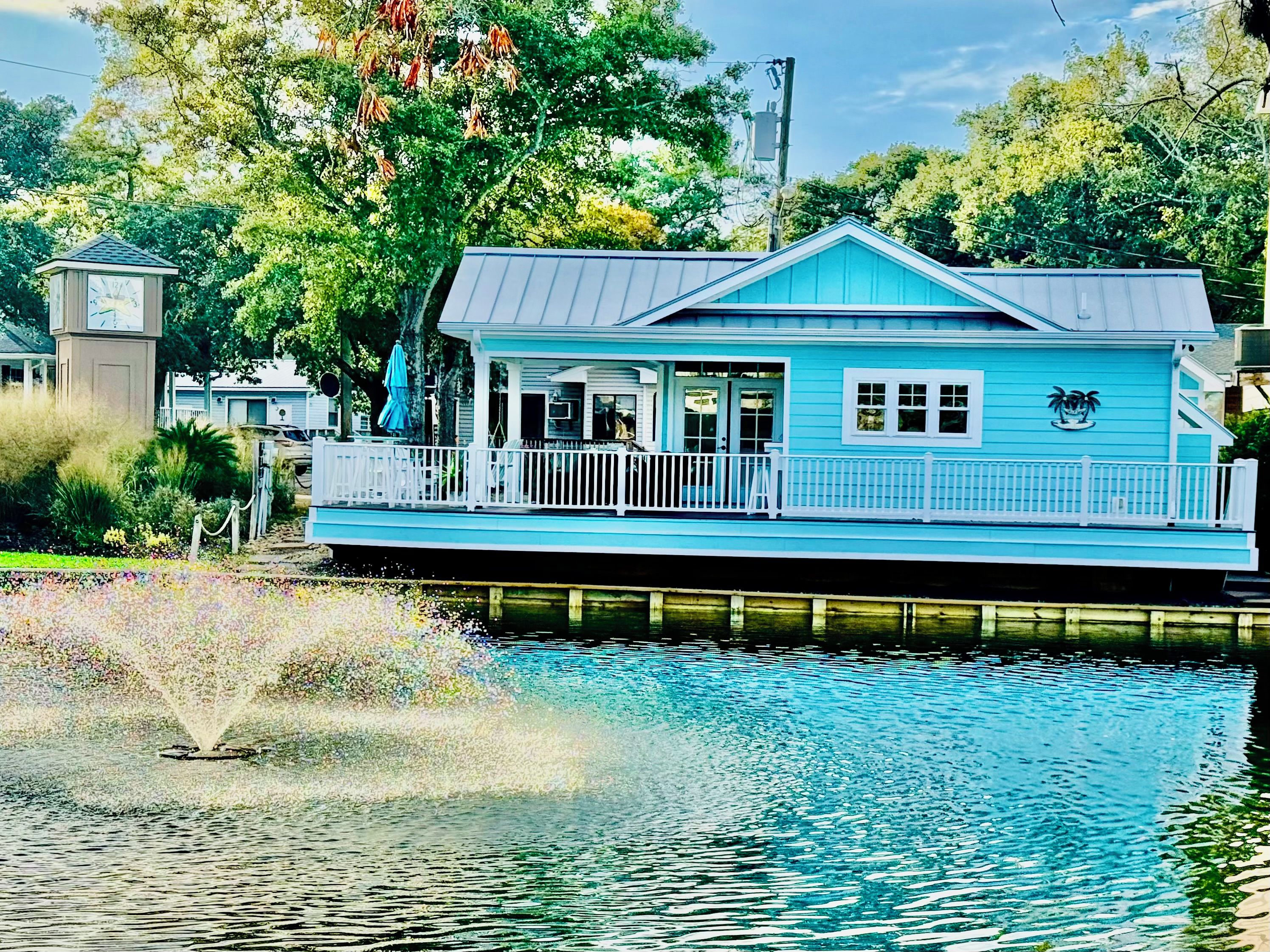 A houseboat with a balcony, a small dock, and a fountain in the foreground.