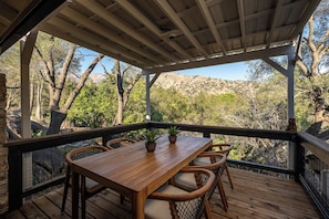 A wooden deck with a table and chairs, surrounded by a metal railing, overlooking a mountainous landscape. - Upscale Sequoia Retreat - Hot Tub, Sauna, & Pool (Three Rivers)