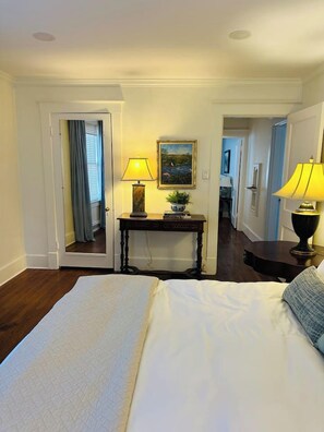 A hotel room with a large bed, a bedside table with a lamp, a mirror, and a painting on the wall. - Luxury 2BR-1BA- Broadway BNB- Walk to Centre (Danville)