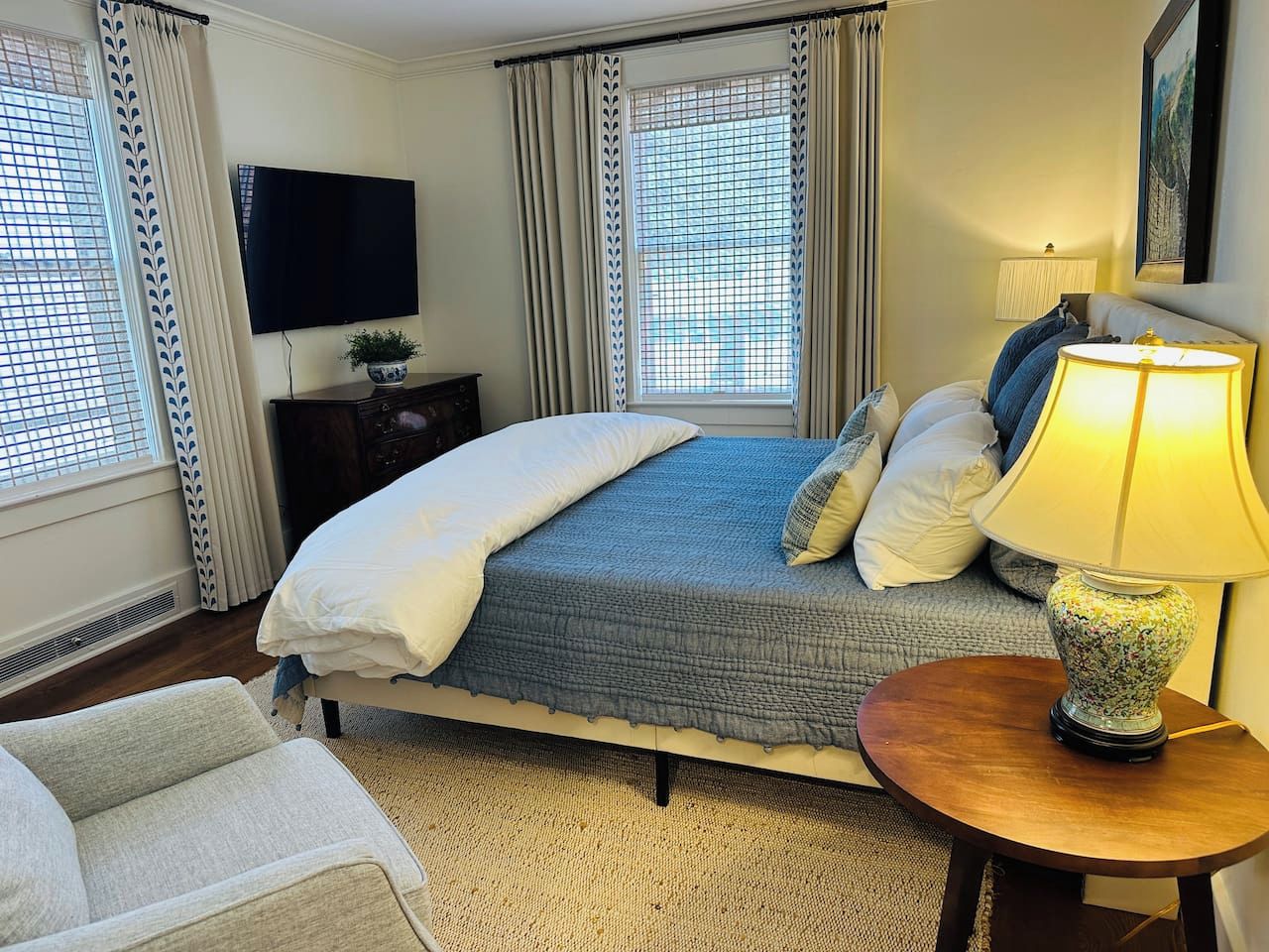 A hotel room with a bed, a TV, a lamp, and a view of the outside through the window.