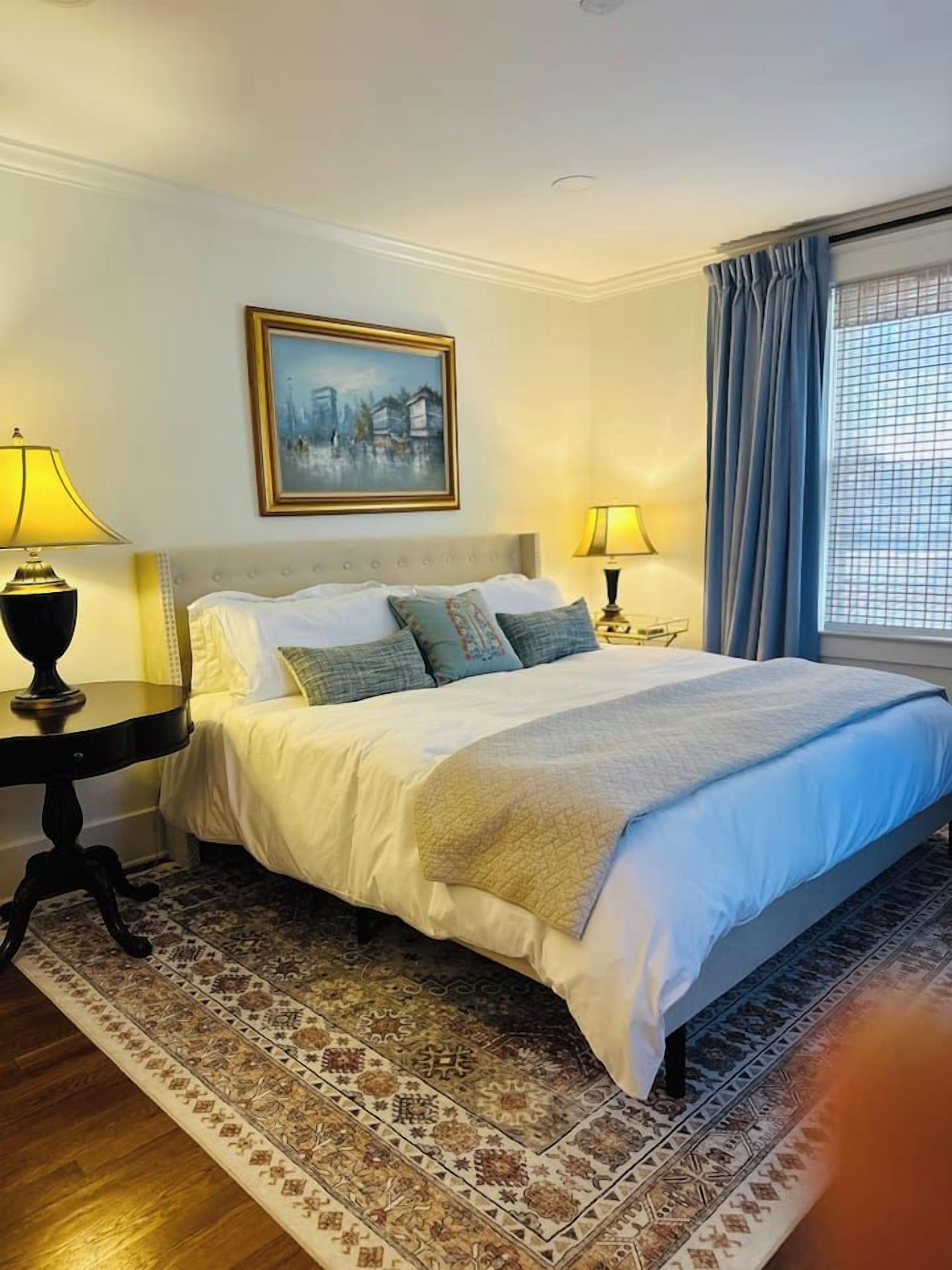 Une chambre d’hôtel avec un grand lit, deux lampes de chevet, un tapis à motifs et un tableau encadré au mur.