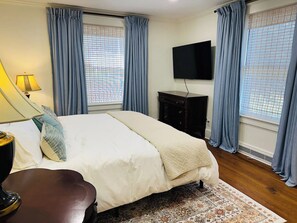 Un dormitorio con cama, televisor, escritorio y una silla.
