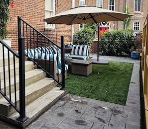 Un patio con escaleras, mobiliario exterior y césped.