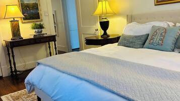 Une chambre à coucher avec un grand lit, deux tables de chevet avec des lampes, un tableau au mur et une porte donnant sur une autre pièce.