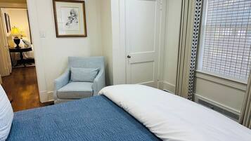 A hotel room with a bed, a chair, a door, and a window with curtains.