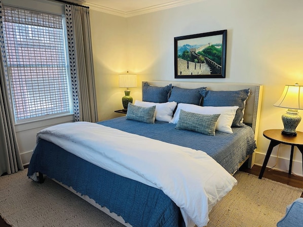 A bedroom with a large bed, two bedside tables, a window with curtains, and a painting on the wall. - Luxury 2BR-1BA- Broadway BNB- Walk to Centre (Danville)