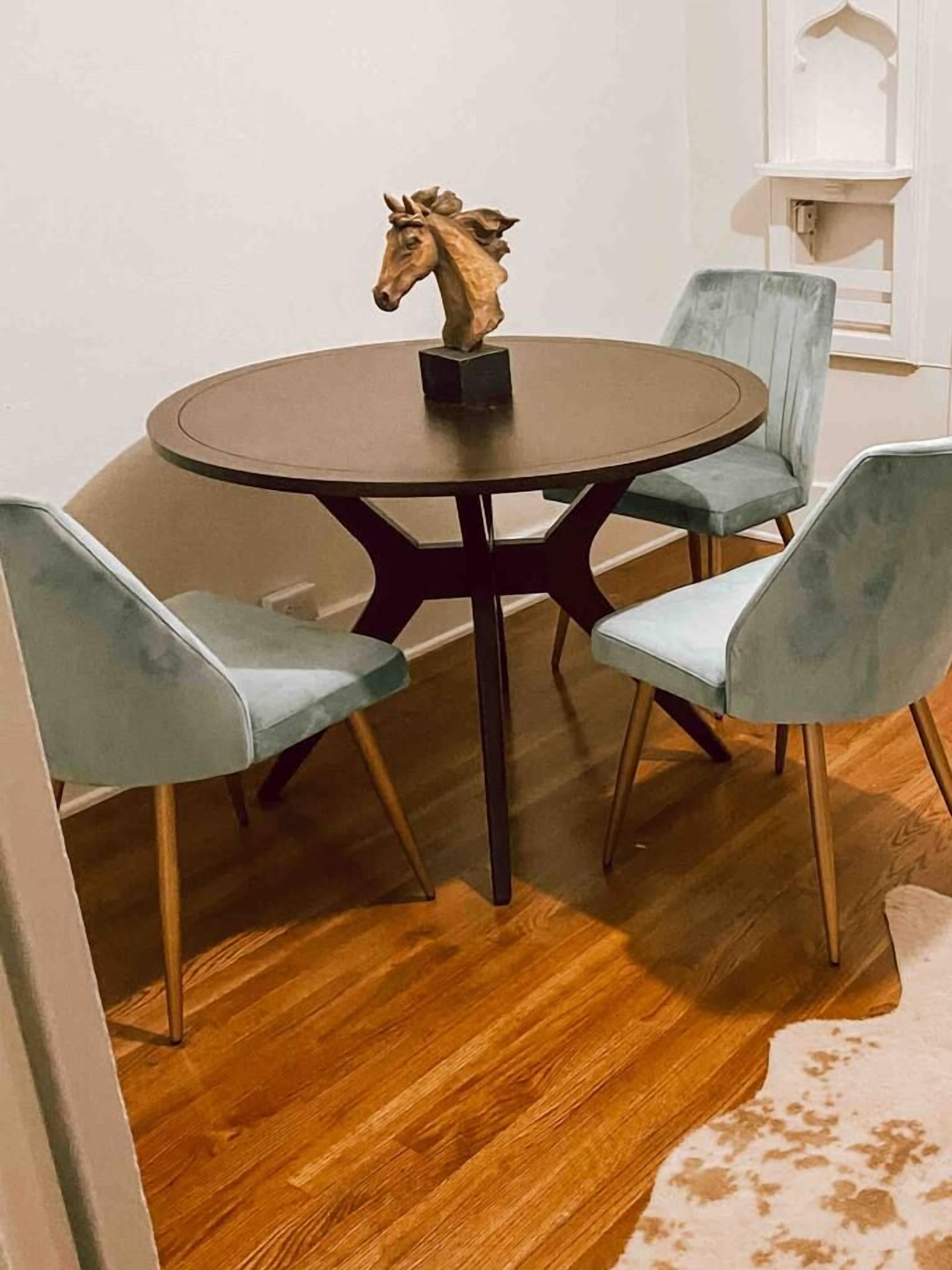 A round table with a horse sculpture centerpiece, surrounded by four light blue chairs with wooden legs.