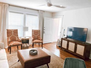 A living room with a sofa, two patterned armchairs, a coffee table, a television on a cabinet, and a door with a number. - Broadway BNBs I - 1 BR Apartment - Walk to Centre (Danville)